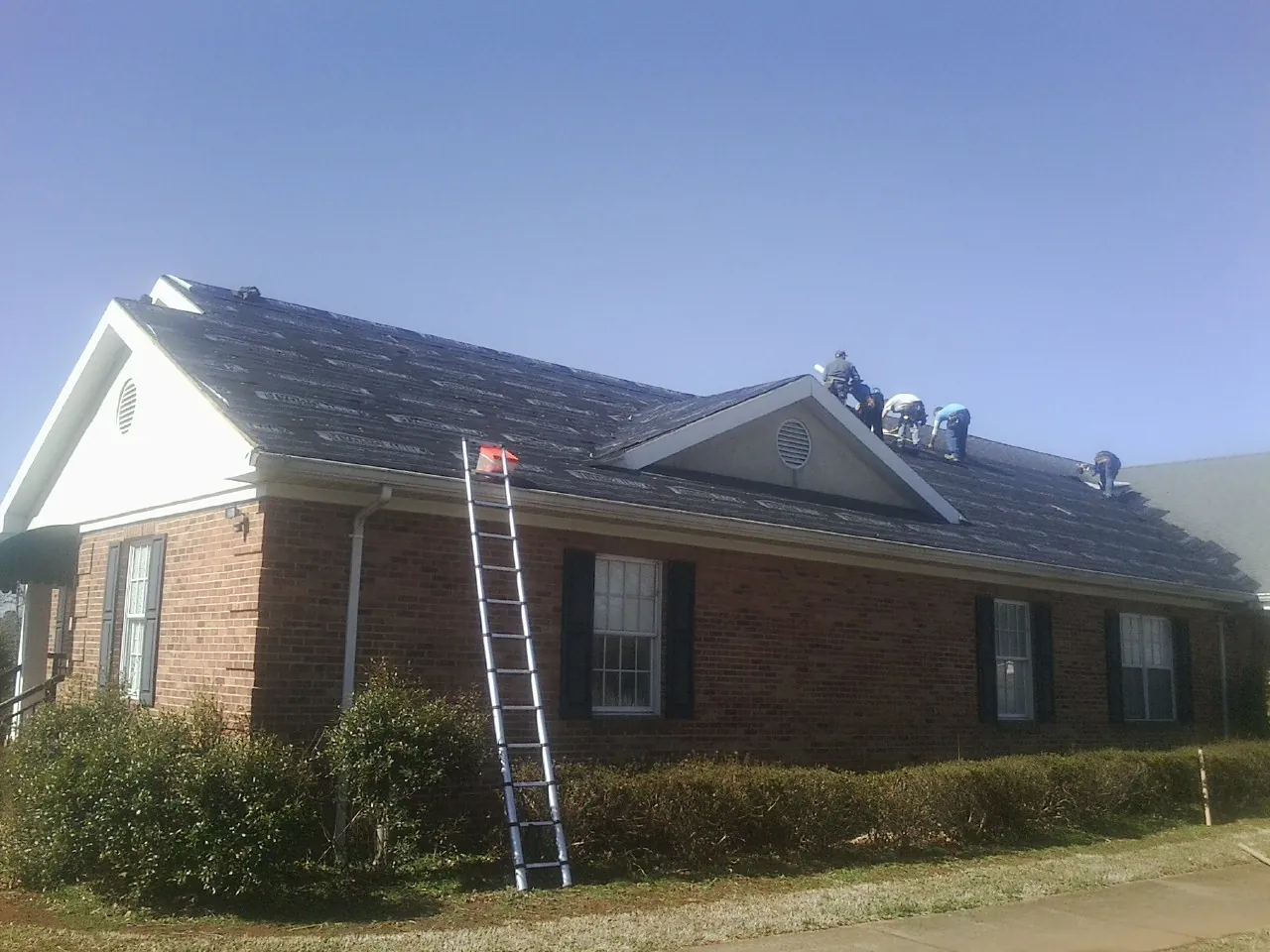 Crew tearing shingles off a brick ranch roof with a ladder set — Metal Roof Repair work by our crew in Brilliant