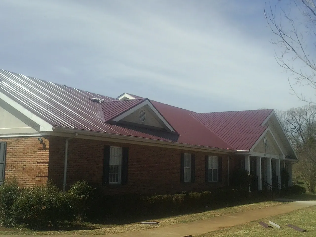 Red metal roof with gabled entries on a long brick building, from a Hail Damage Roof Repair job in Brilliant
