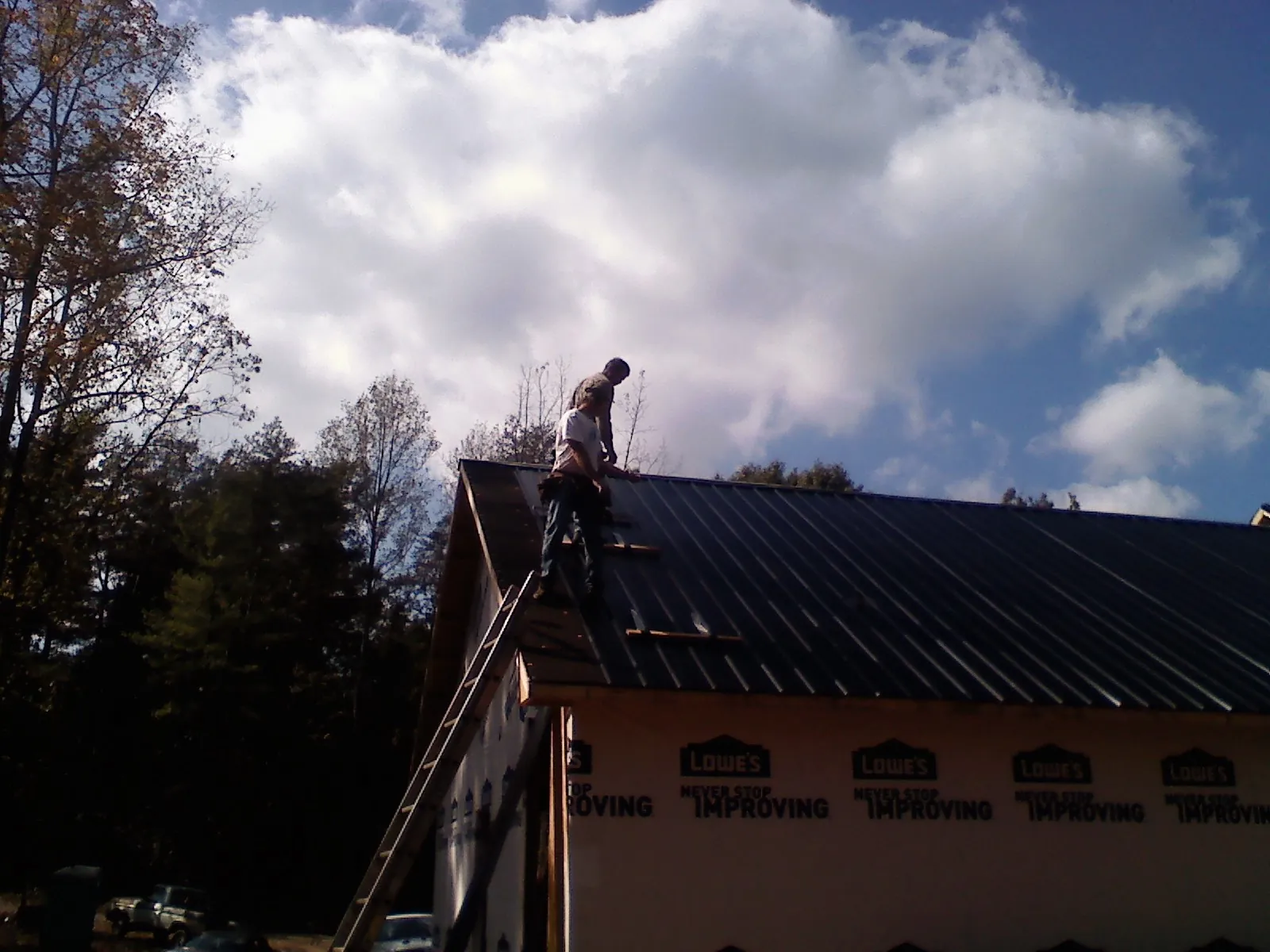 Roofer fastening dark metal panels high against a cloudy sky, from a Roof Inspection job in Brilliant